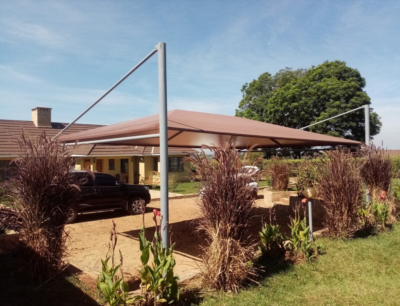 Finished maroon tensile cantilever car parking shade structure at a residential property in Kitale, wide view