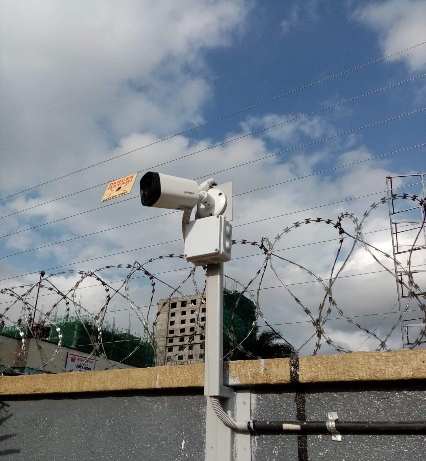 Dahua bullet CCTV camera mounted on a pole above a razor-wire-topped perimeter wall in Muthaiga, with an electric fence danger sign visible