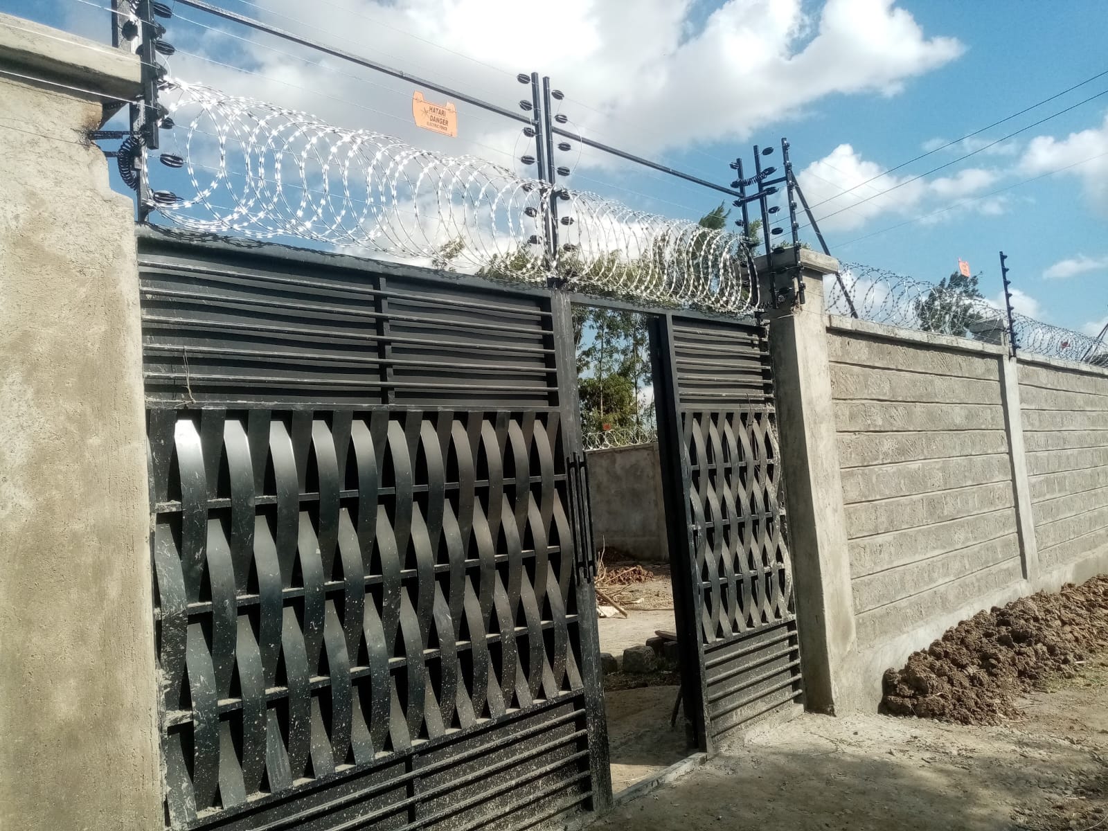 Close-up of electric fence posts, razor wire, and a decorative woven-steel gate at a Ruiru property entrance