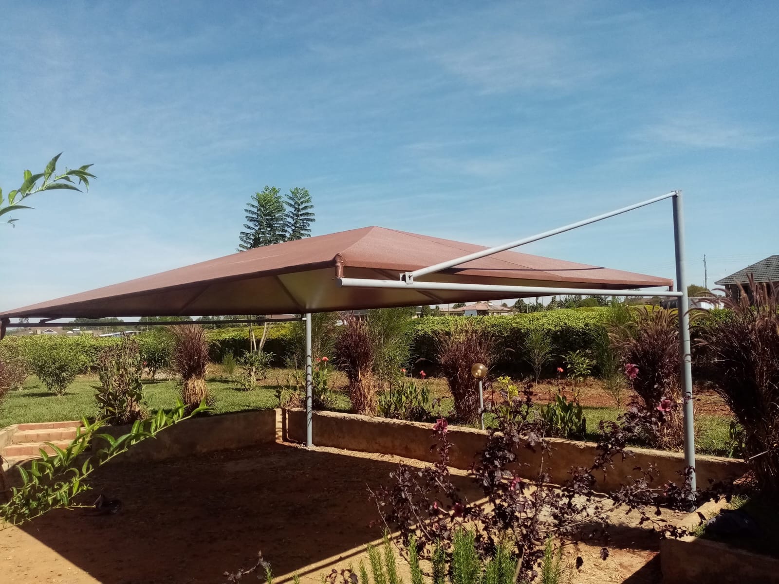Finished maroon cantilever car parking shade structure in Kitale, alternate angle showing garden landscaping