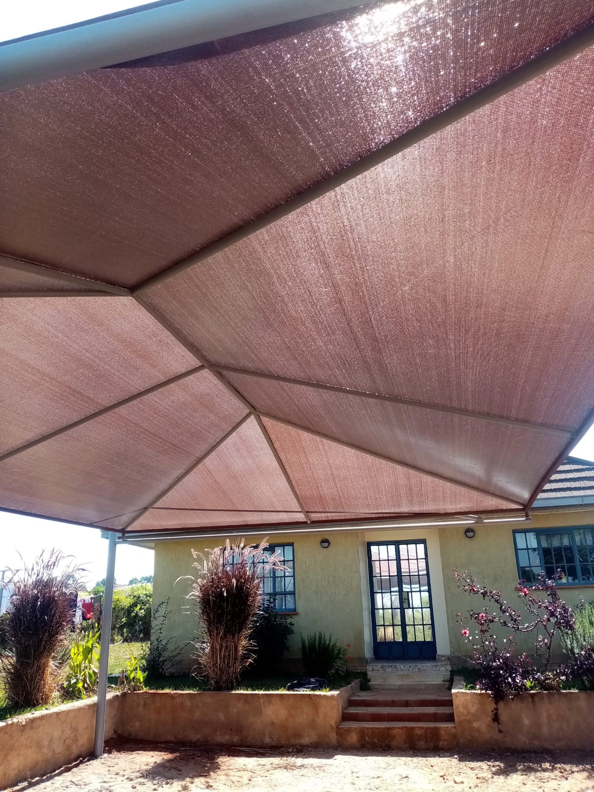 Close-up of the tensile fabric weave and steel framing underside of a car parking shade structure in Kitale
