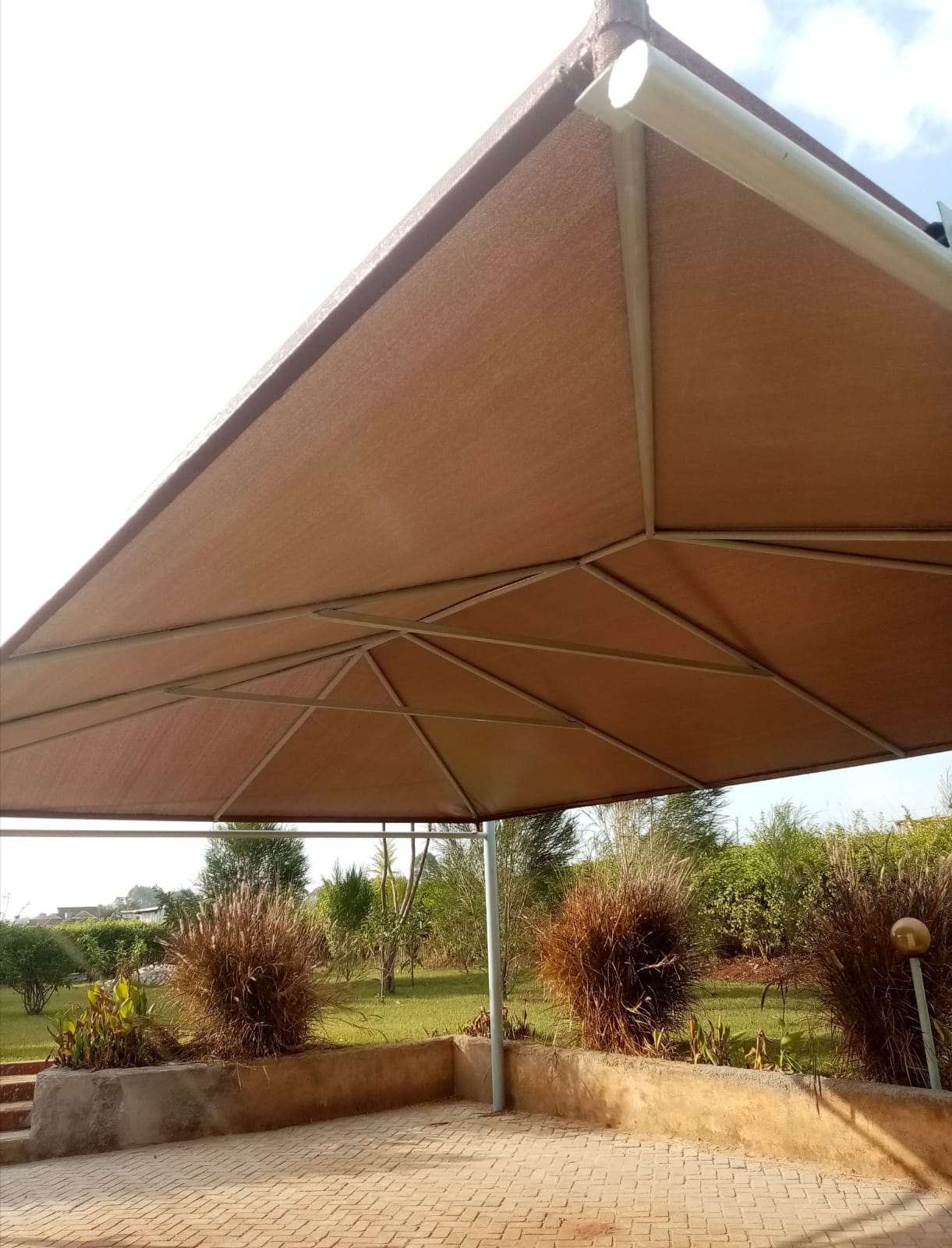 Finished maroon cantilever car parking shade structure in Thika, alternate underside angle with garden landscaping