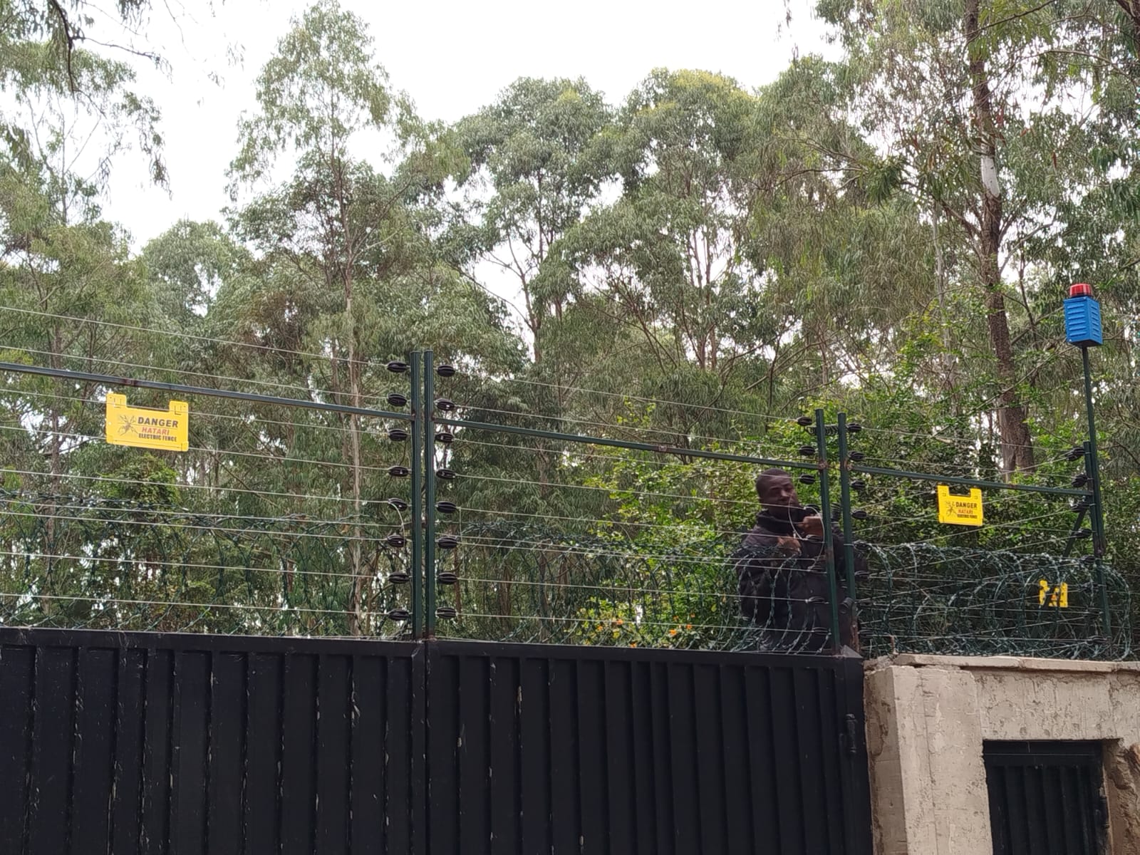 Technician working at a gate integrated with electric fence and razor wire on a Karen boundary wall